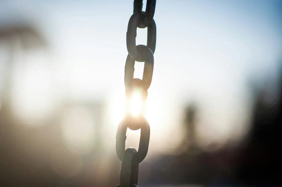 A steel chain hanging vertically against the light, with the low sun shining through one of the links