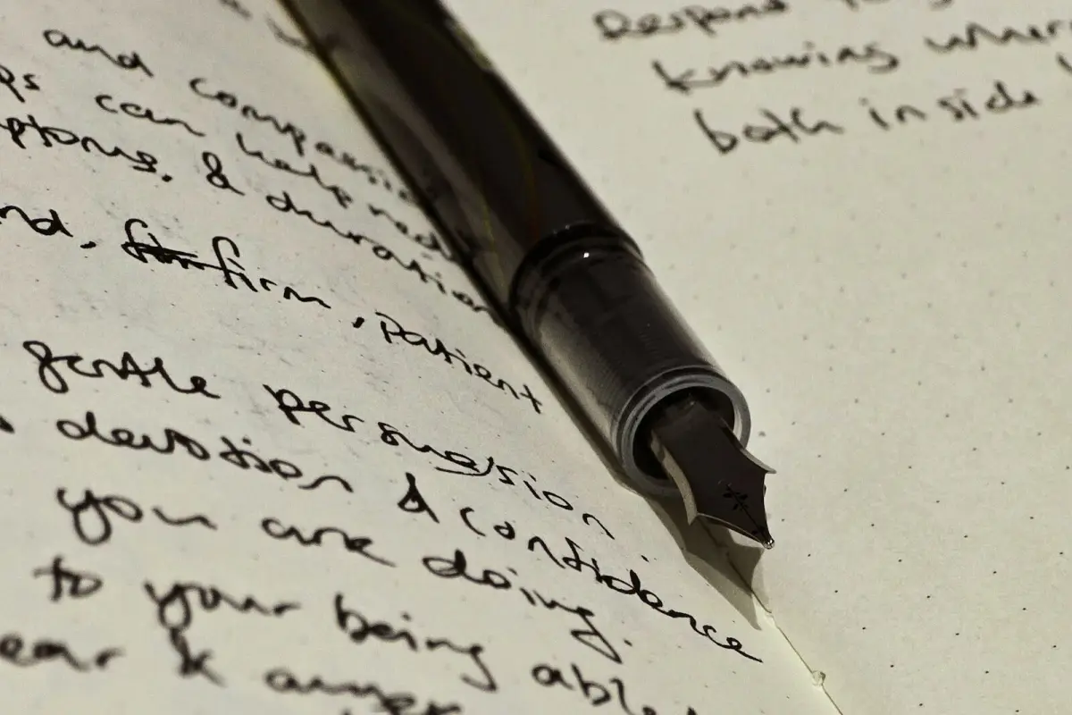A black fountain pen lying at an angle across the closely handwritten pages of an open notebook