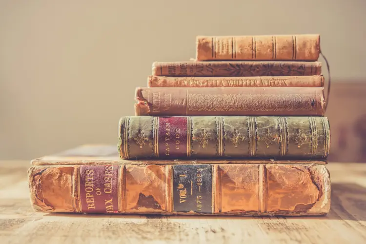 Sechs alte, in Leder gebundene Bücher unterschiedlicher Größe liegen gestapelt auf einem Holztisch, unten der größte Band, oben der kleinste
