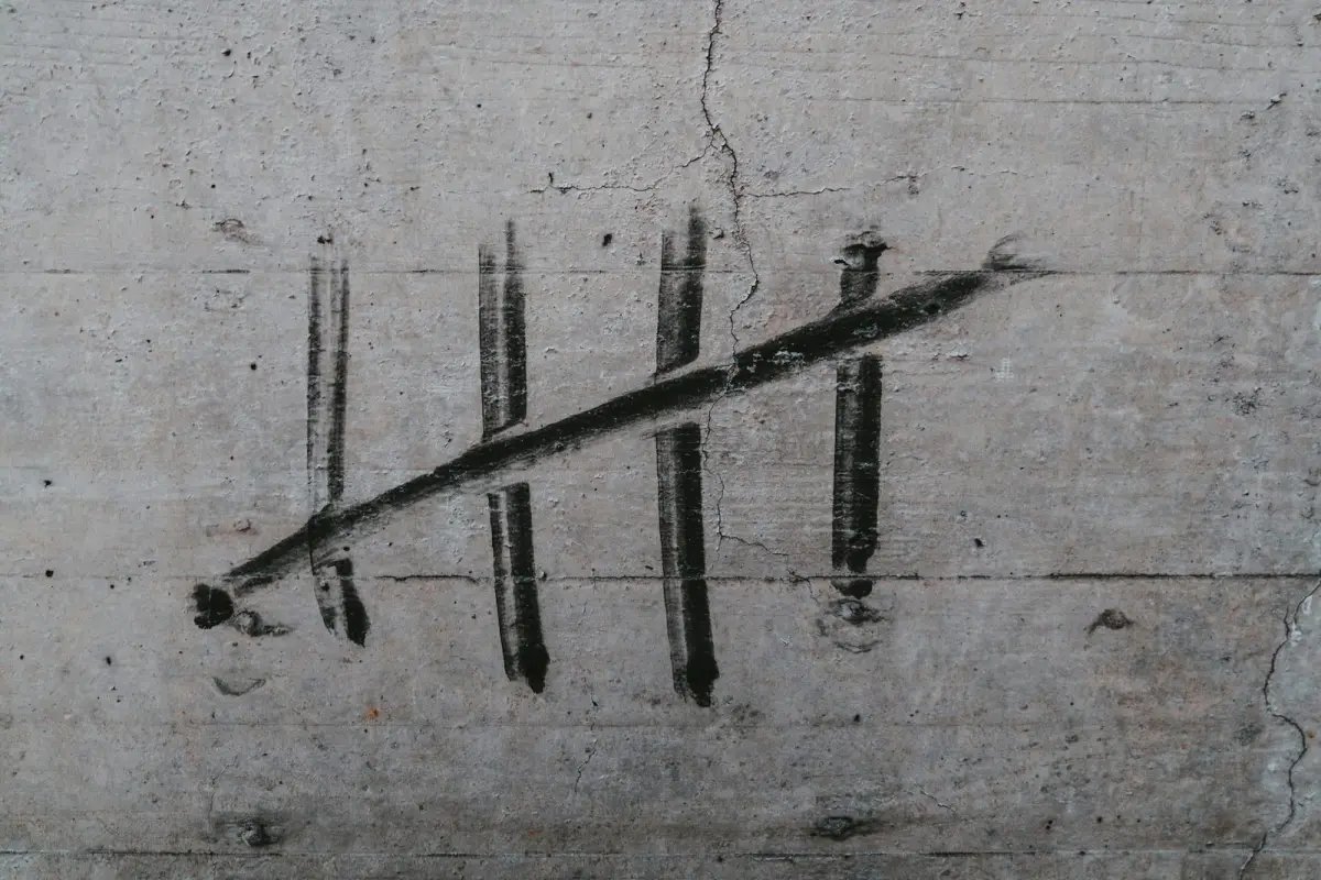 Five tally marks painted in black on a concrete wall, the fifth struck diagonally across the other four