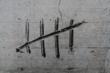 Five tally marks painted in black on a concrete wall, the fifth struck diagonally across the other four