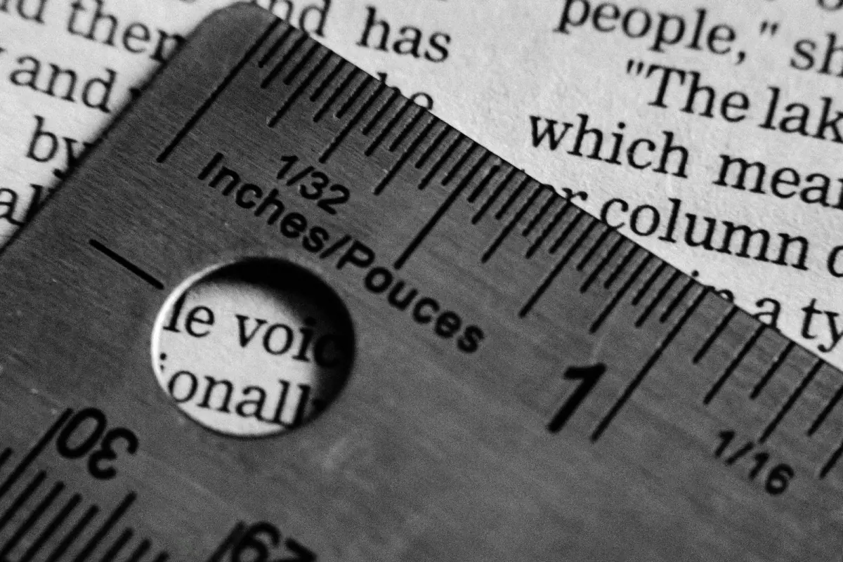 A metal ruler with inch and centimetre scales lying at an angle across a printed page, single words visible through a hole in the ruler